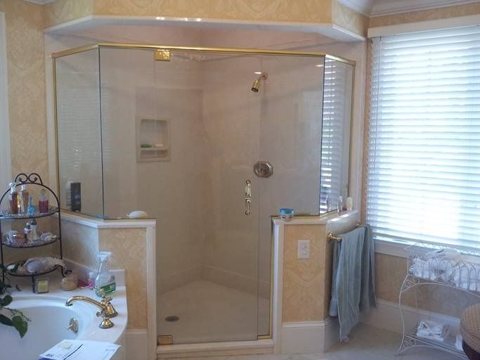 Bathroom with a glass shower, beige walls, and a window with blinds.