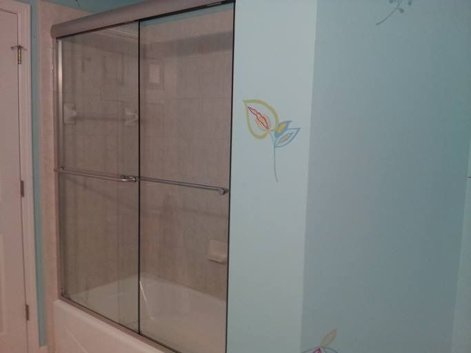 A bathroom with a glass shower door over a bathtub. Light blue walls with leaf drawings.