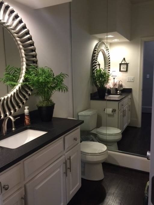 Bathroom with white cabinets, black countertop, round mirrors, and a potted plant.