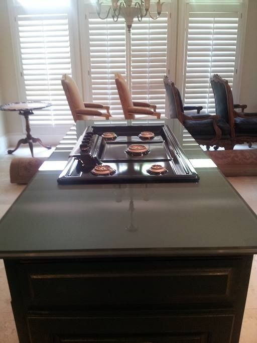 Kitchen island with stovetop, dark countertops, and cabinets. Windows and chairs in background.
