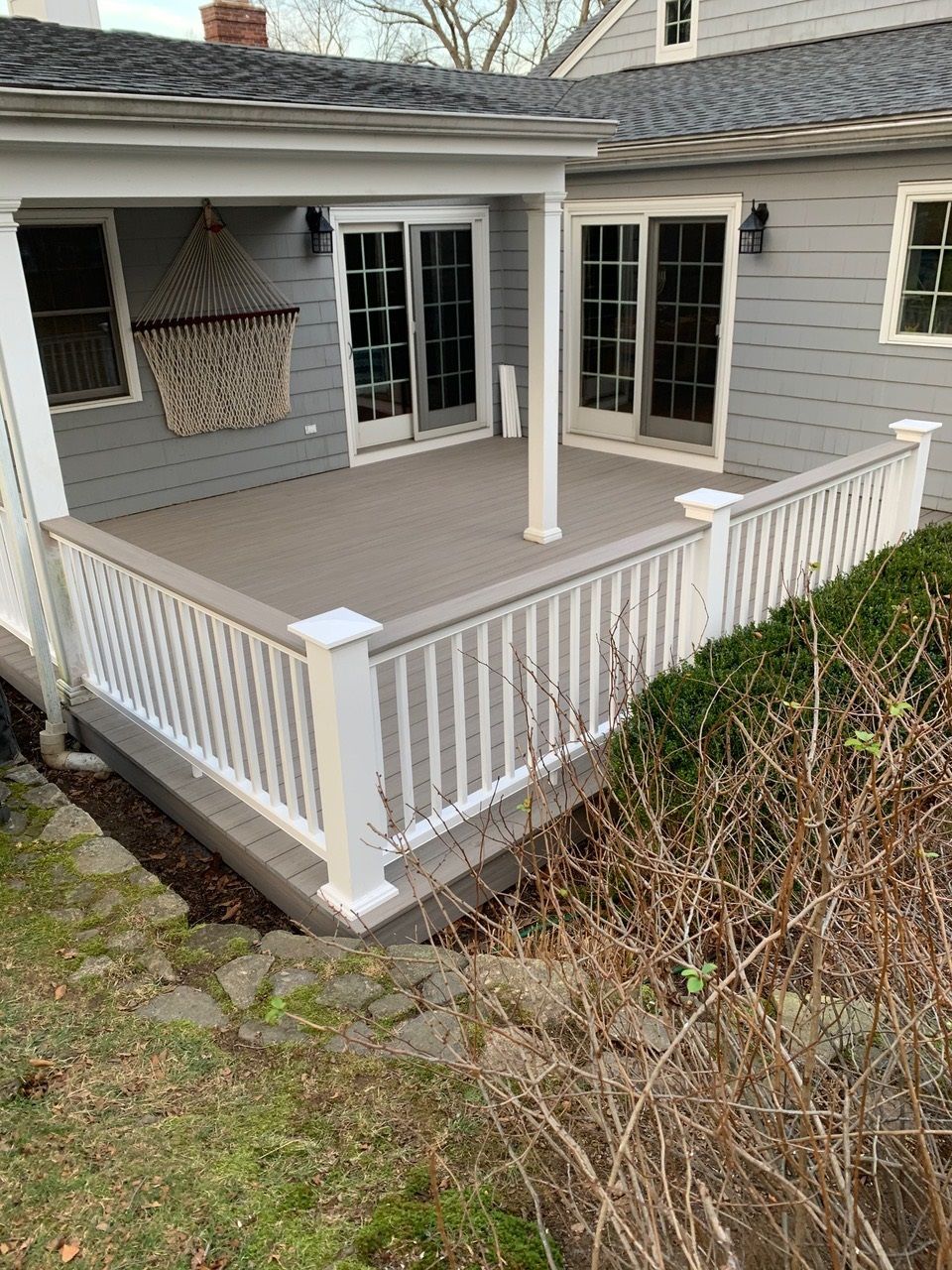 A large porch with a white railing and sliding glass doors on the side of a house