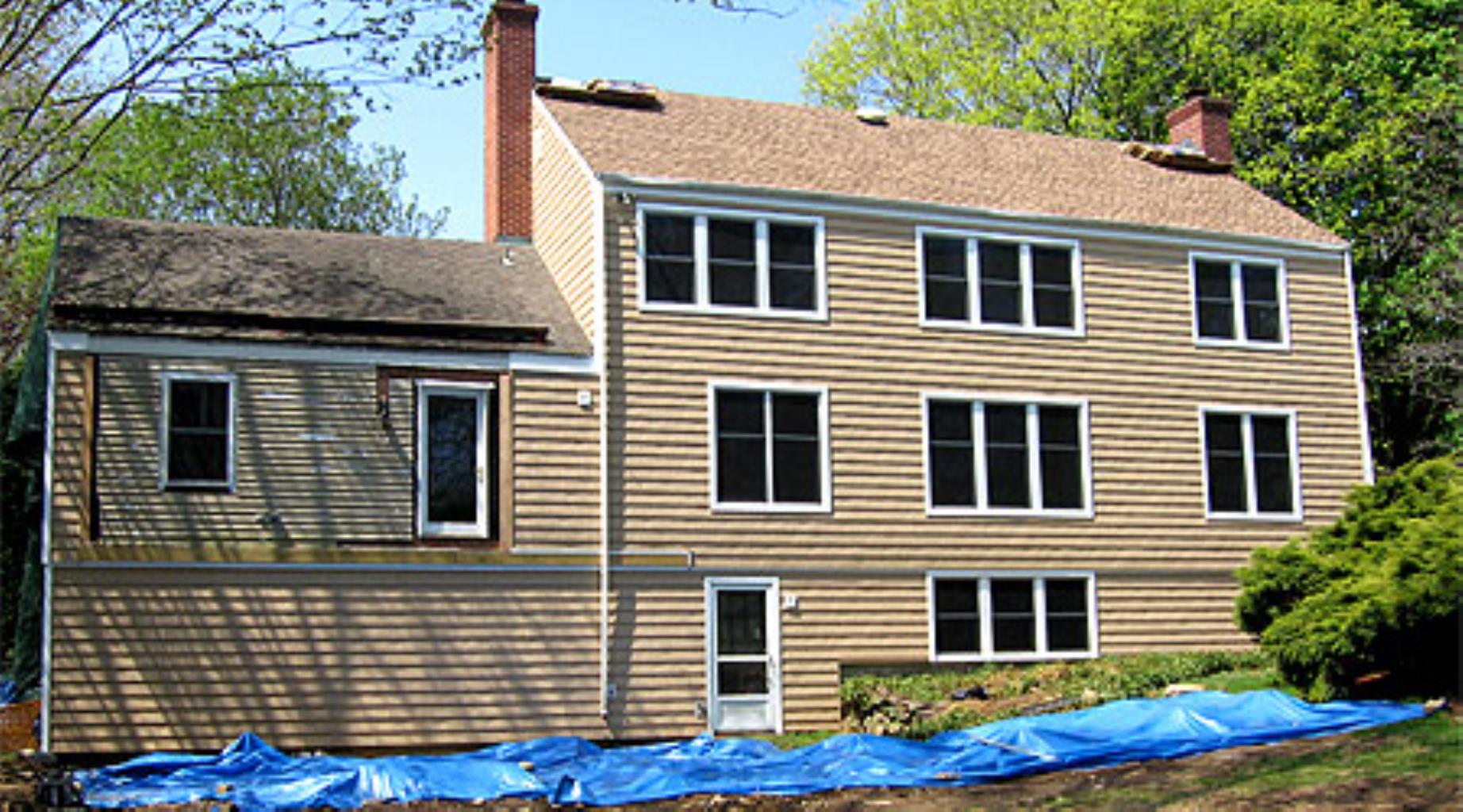 A large house with a lot of windows is covered in blue tarps
