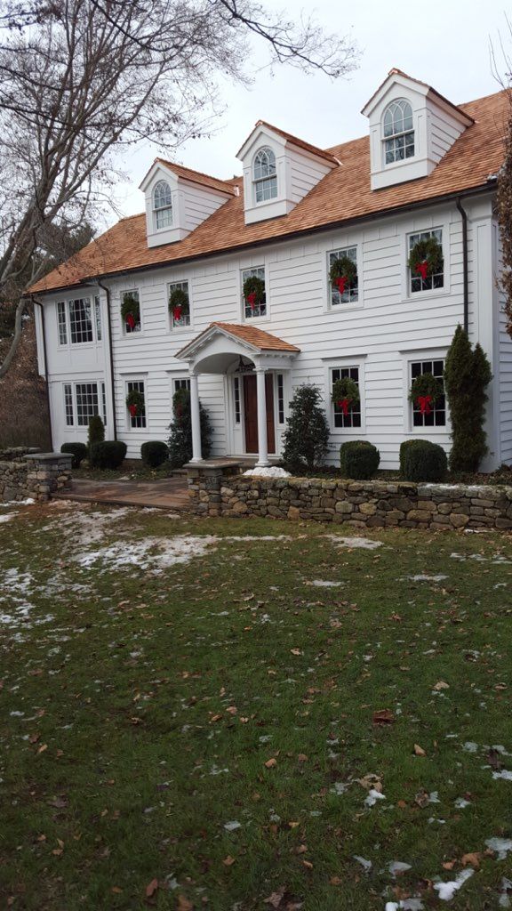 A large white house with a wooden roof and Christmas wreaths on the windows