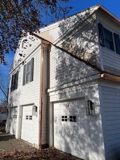 A white house with two garage doors and a copper gutter