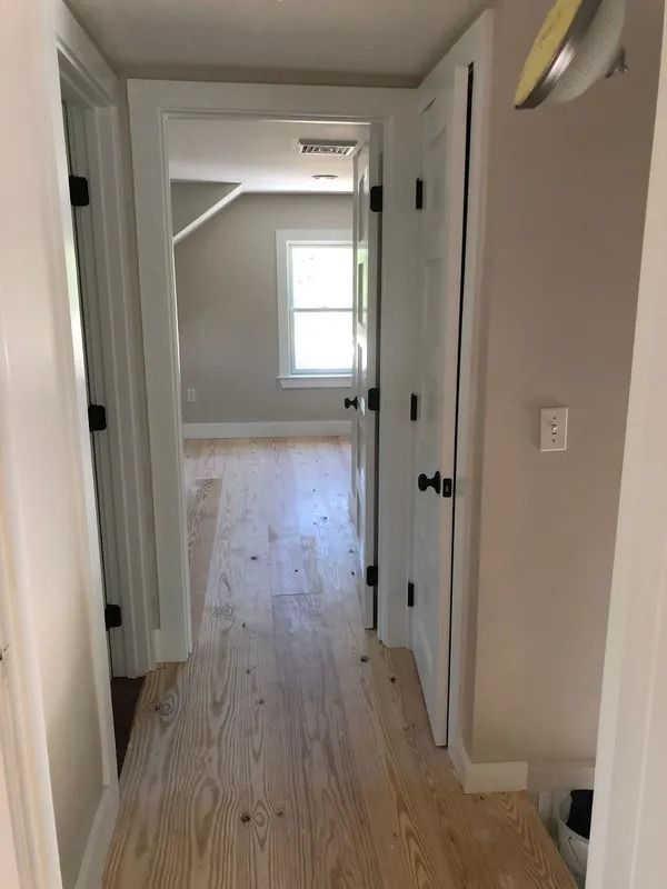 Hallway with light wood floors, leading to a room with a window. White doors, gray walls, black door hardware.