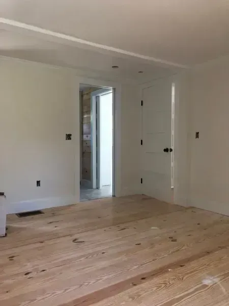 Empty room with light wood floors, white walls, and a doorway leading to another room.