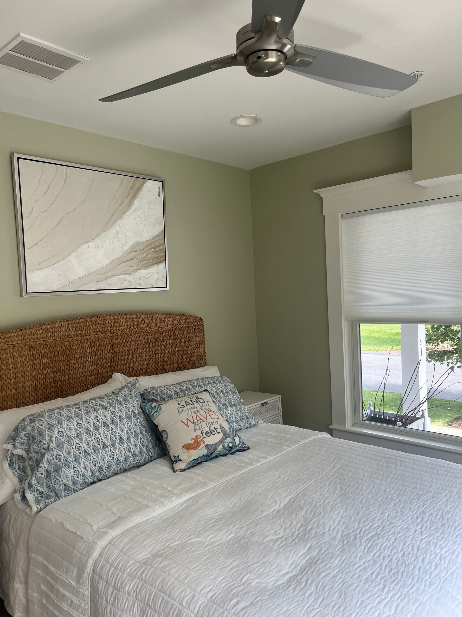 Bedroom with bed, wicker headboard, pillows, framed art, and a ceiling fan.