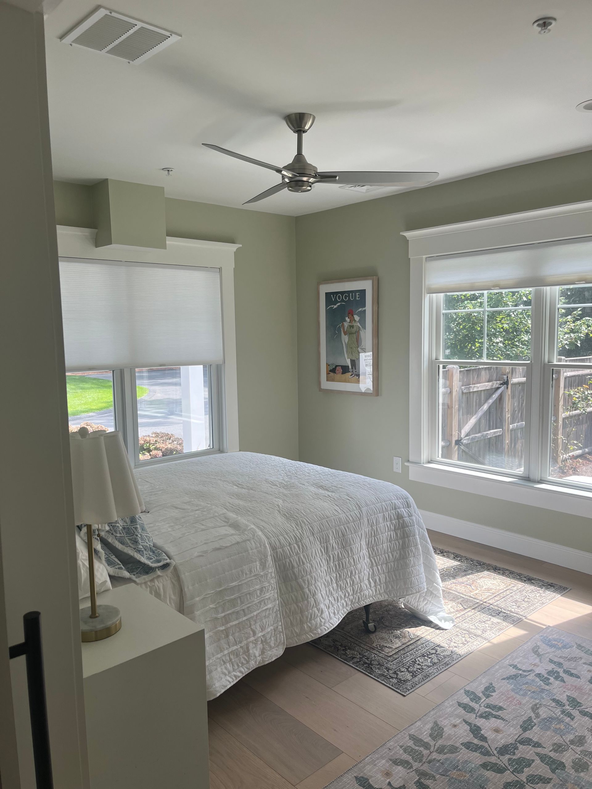 Bedroom with white bedding, pale green walls, and large windows.