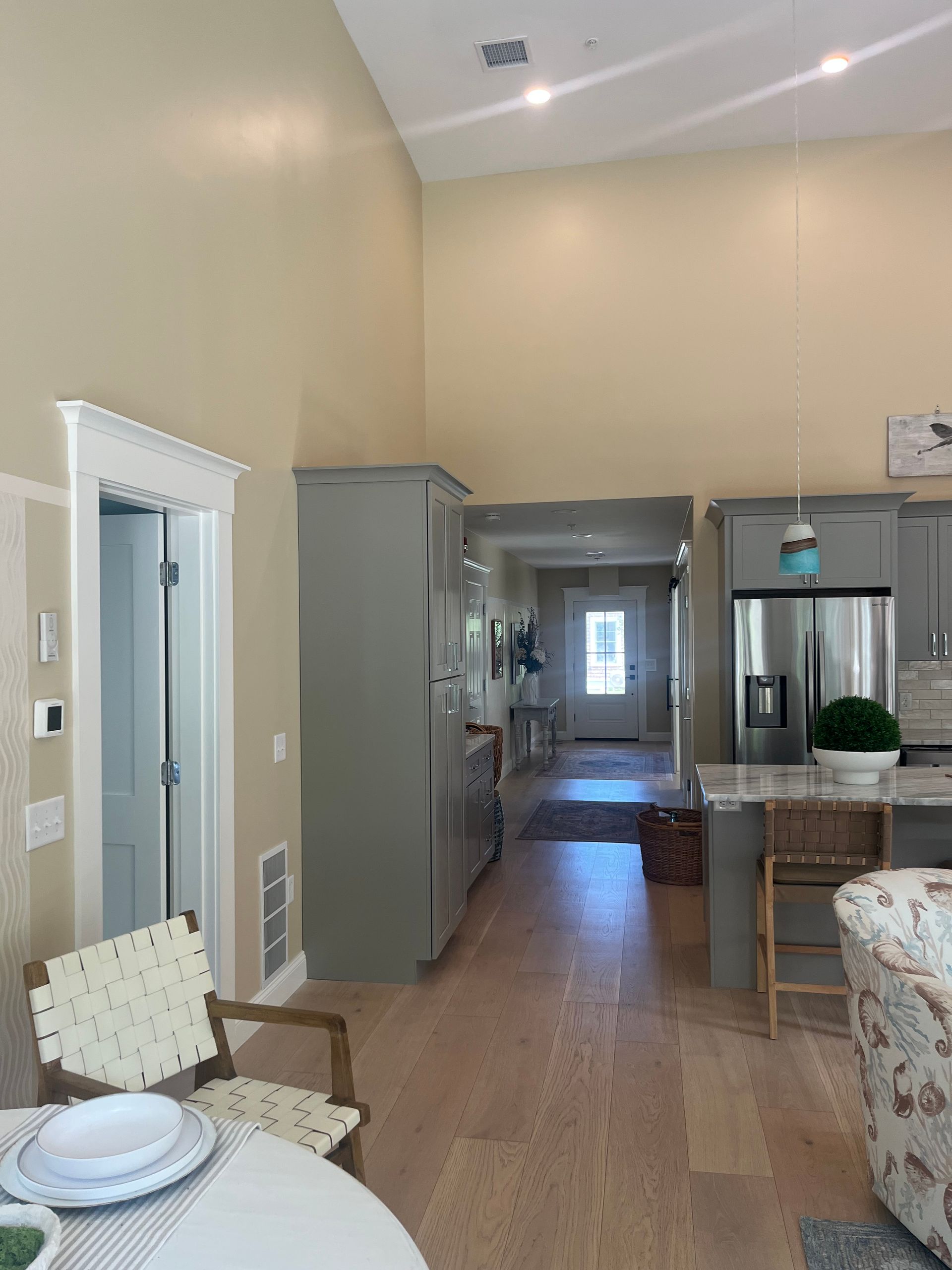 Interior view of a light-filled home with high ceilings, featuring a kitchen, dining area, and hallway with wooden floors.