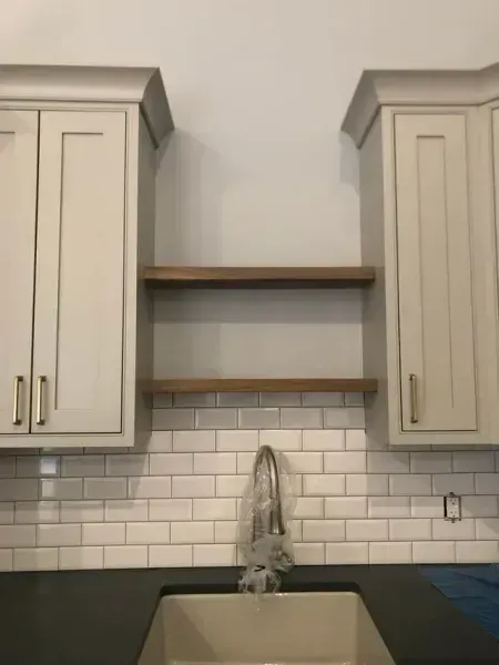 Kitchen with gray cabinets, subway tile backsplash, dark countertop, and wooden shelves.