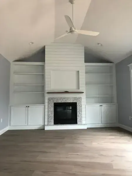 Living room with fireplace, white built-in shelves and cabinets, white ceiling fan, and light gray walls.