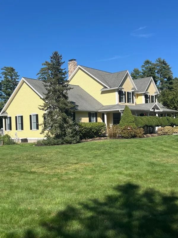 Yellow house with black shutters, green lawn, and blue sky.