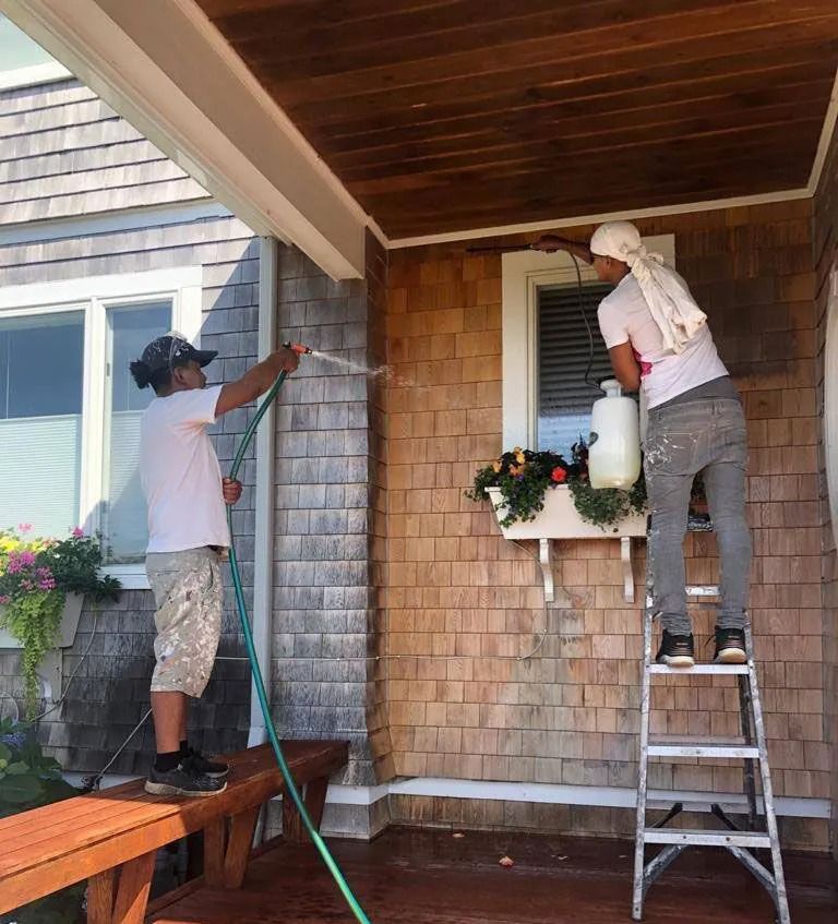 Two people cleaning a house exterior with a hose and sprayer.