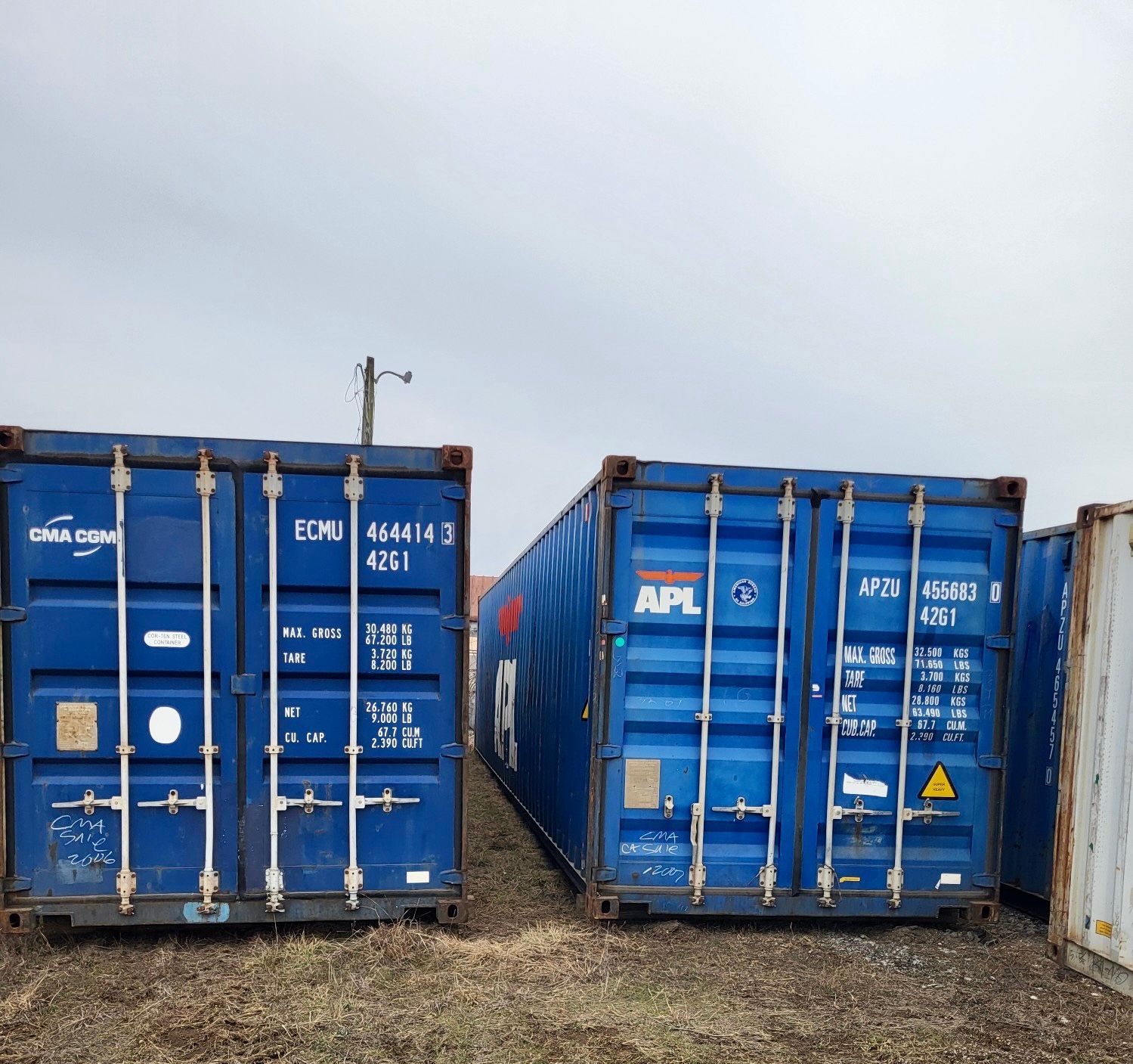 A row of blue shipping containers are lined up in a field