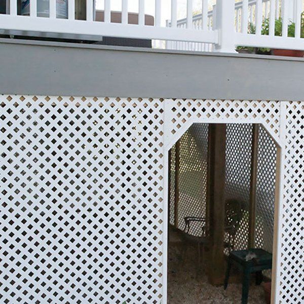 A white lattice fence surrounds a balcony with a table and chairs.
