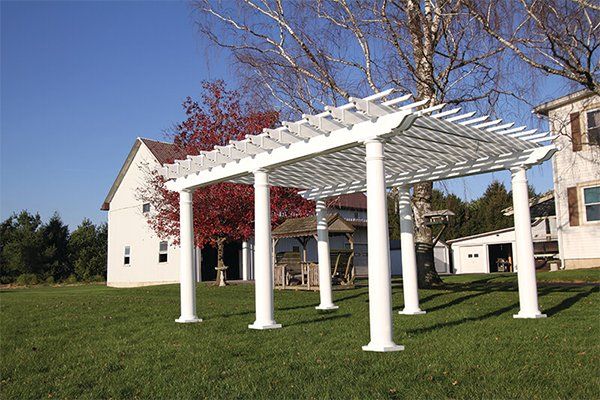 A white pergola is sitting in the grass in front of a house.