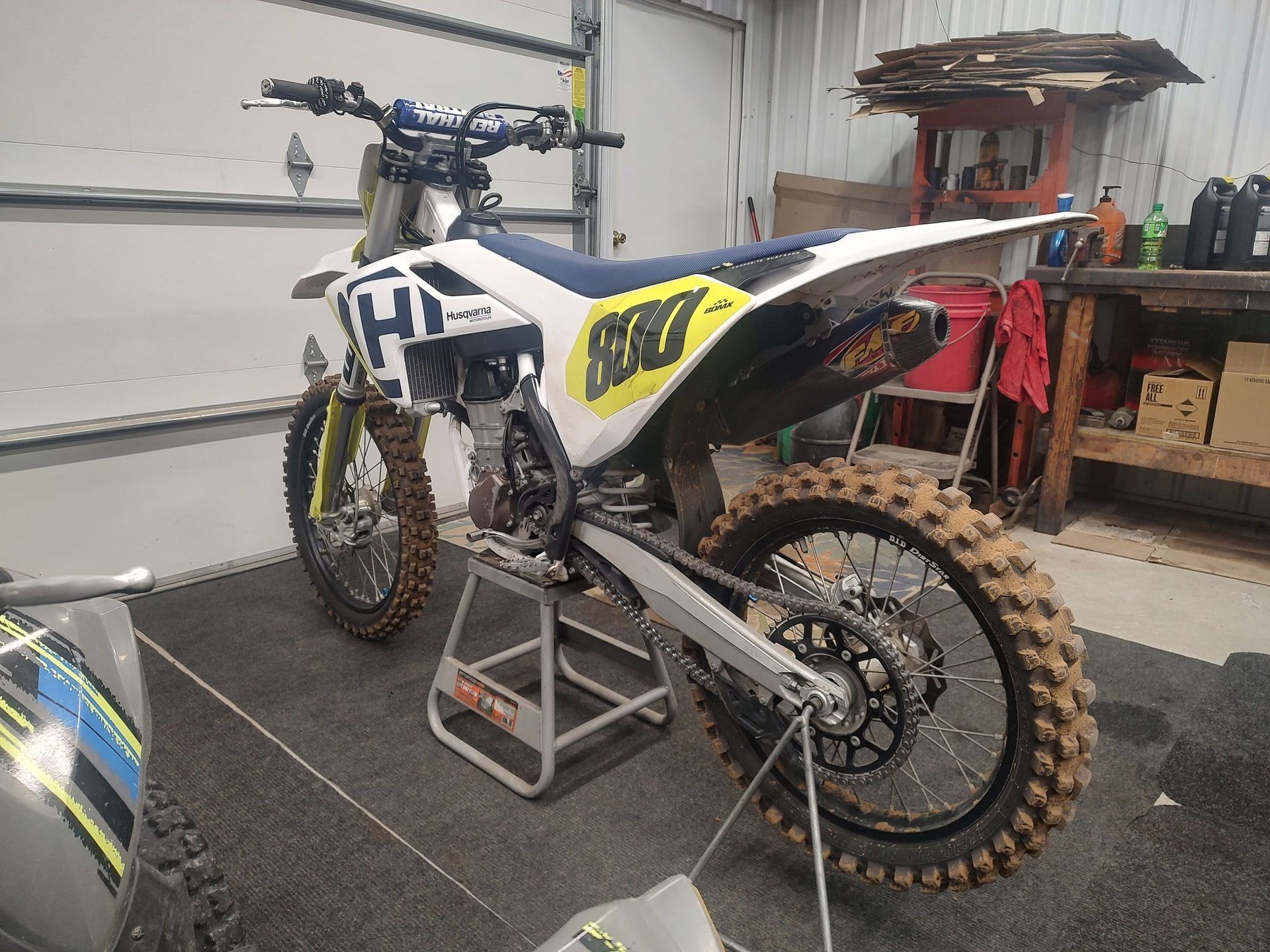 Dirt bike, Husqvarna, parked in a garage. Muddy tires, white and yellow body.