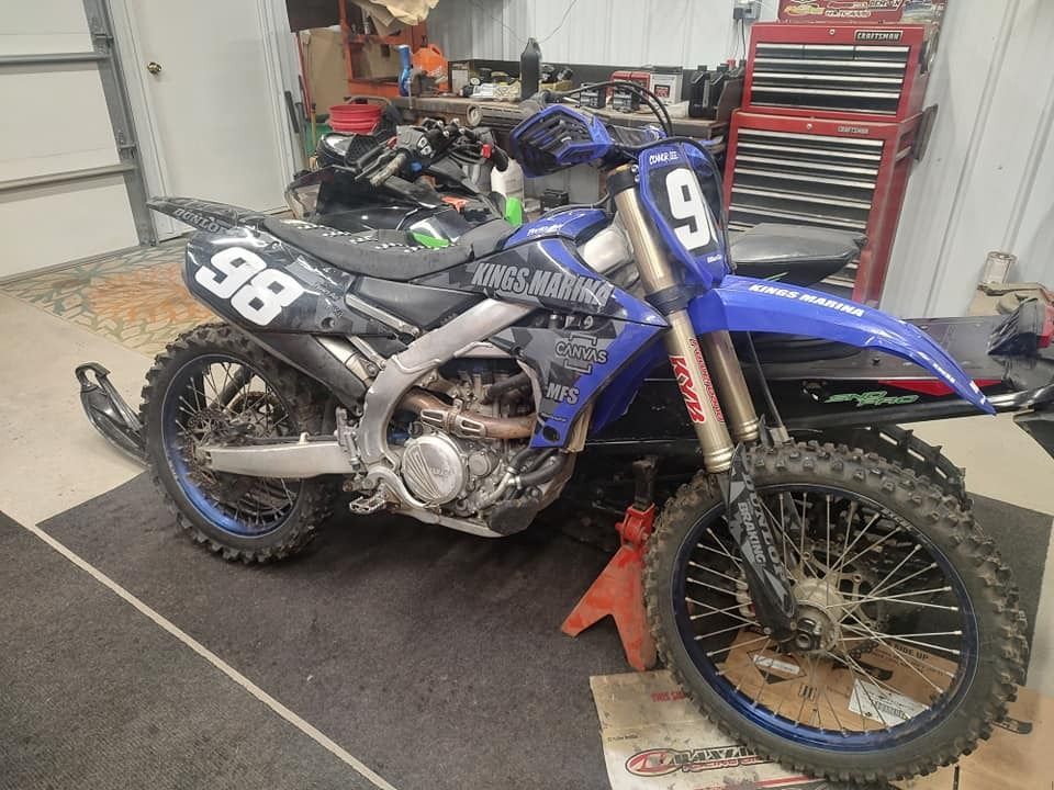 Blue and silver dirt bike with number 9 and 98 on it, propped up in a garage.