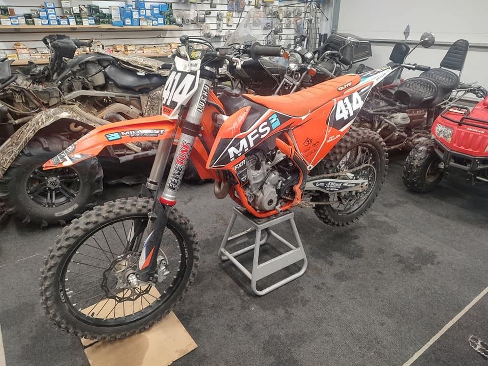 Orange and white motocross bike with number 414 on display in a garage.