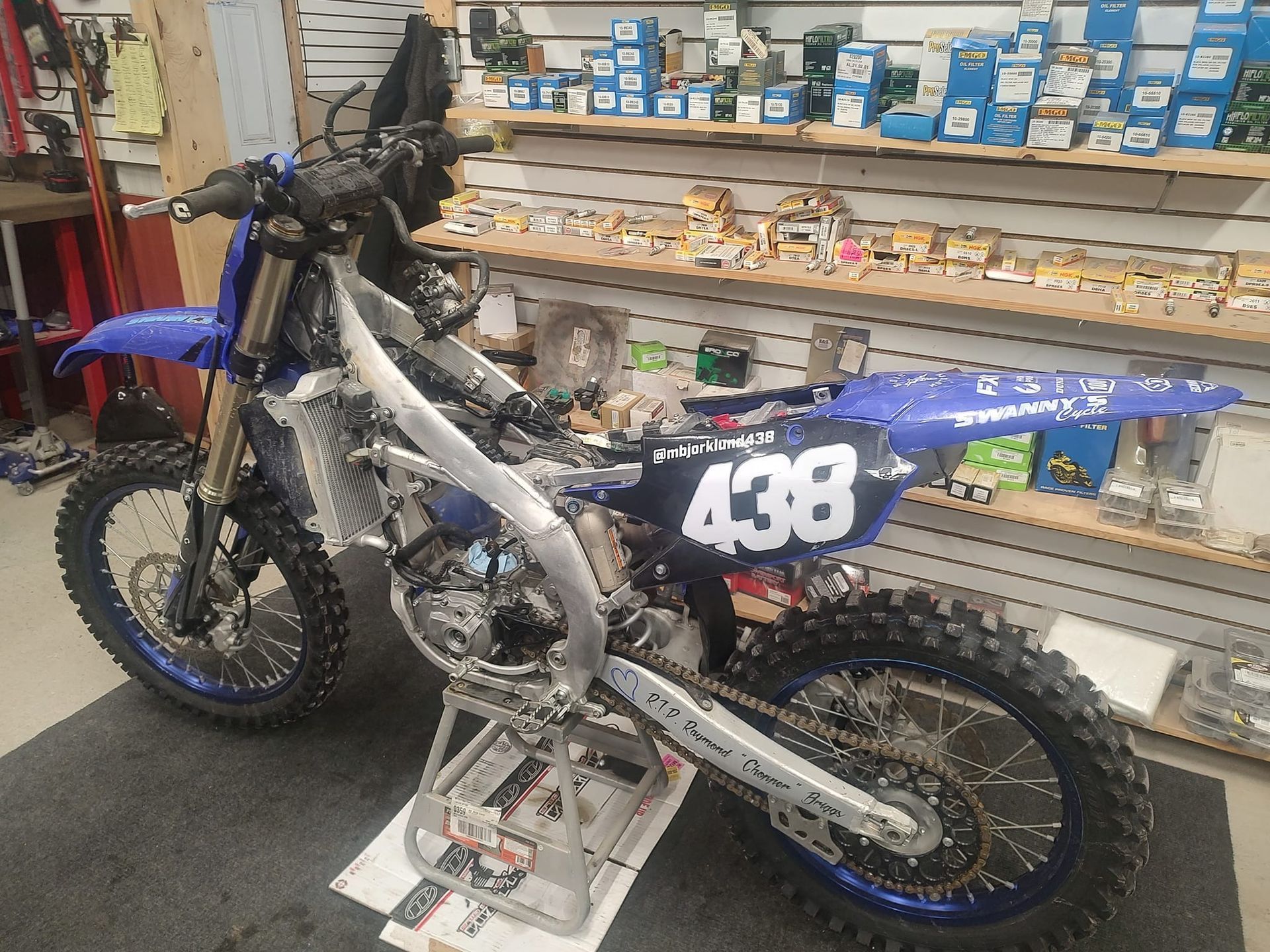 A blue and white Yamaha dirt bike is partially disassembled in a shop.