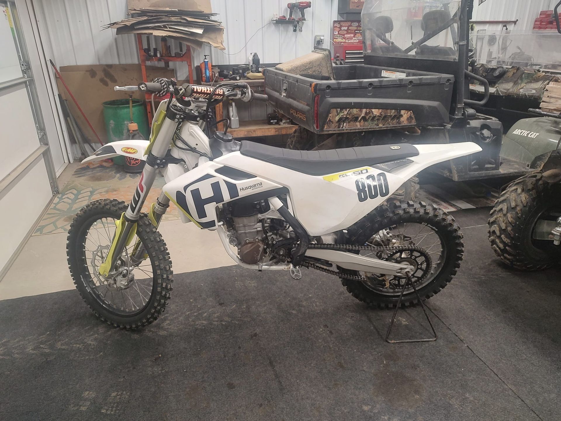 White Husqvarna dirt bike in a cluttered garage, angled view.