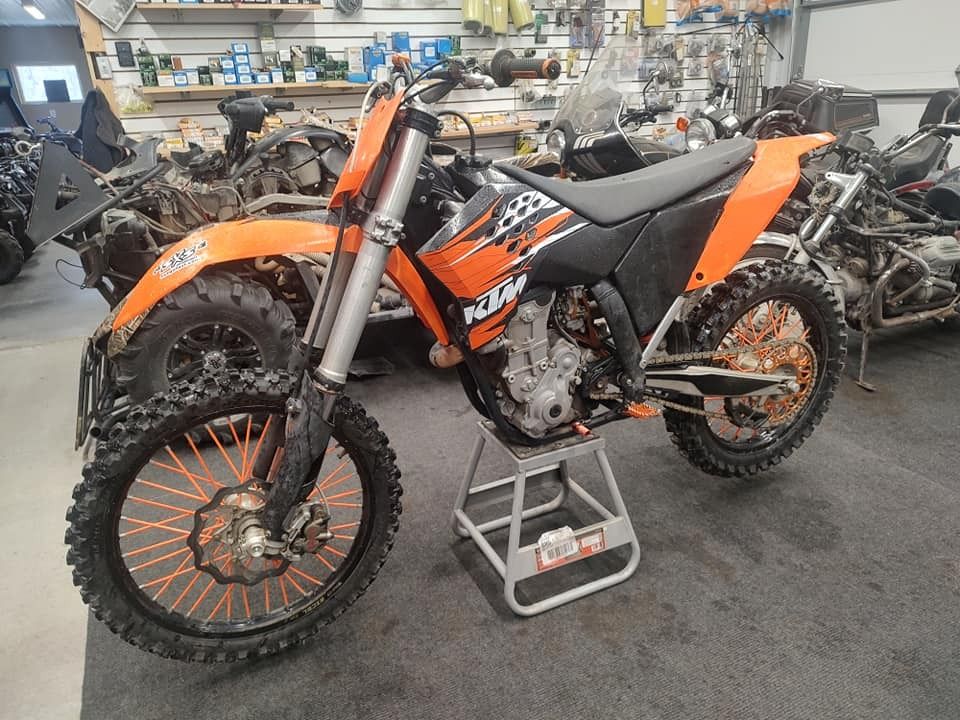 Orange KTM dirt bike on a stand in a workshop, surrounded by parts.