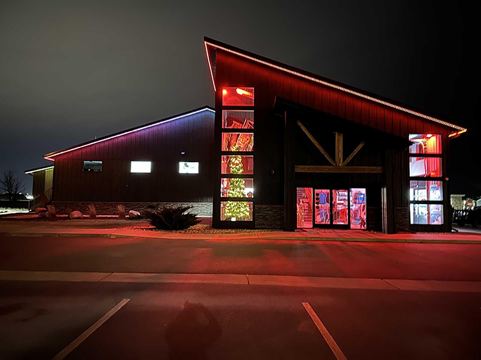 Modern building at night with red-lit facade and large glass entrance, viewed from a parking lot