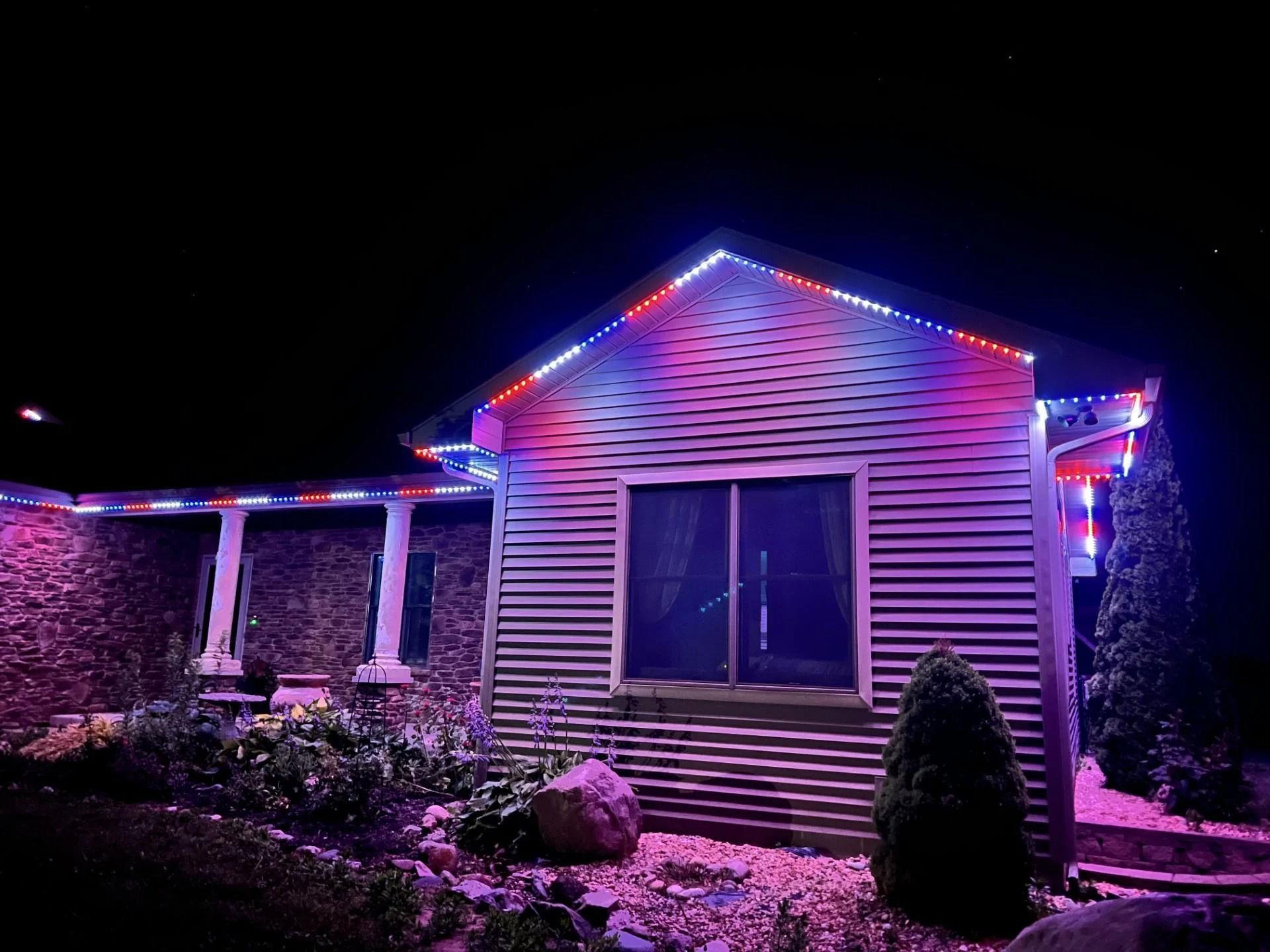 Small house at night with purple and red string lights illuminating the roof and front porch.