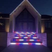 House entrance at night with illuminated red, blue, and white steps and a peaked roof.