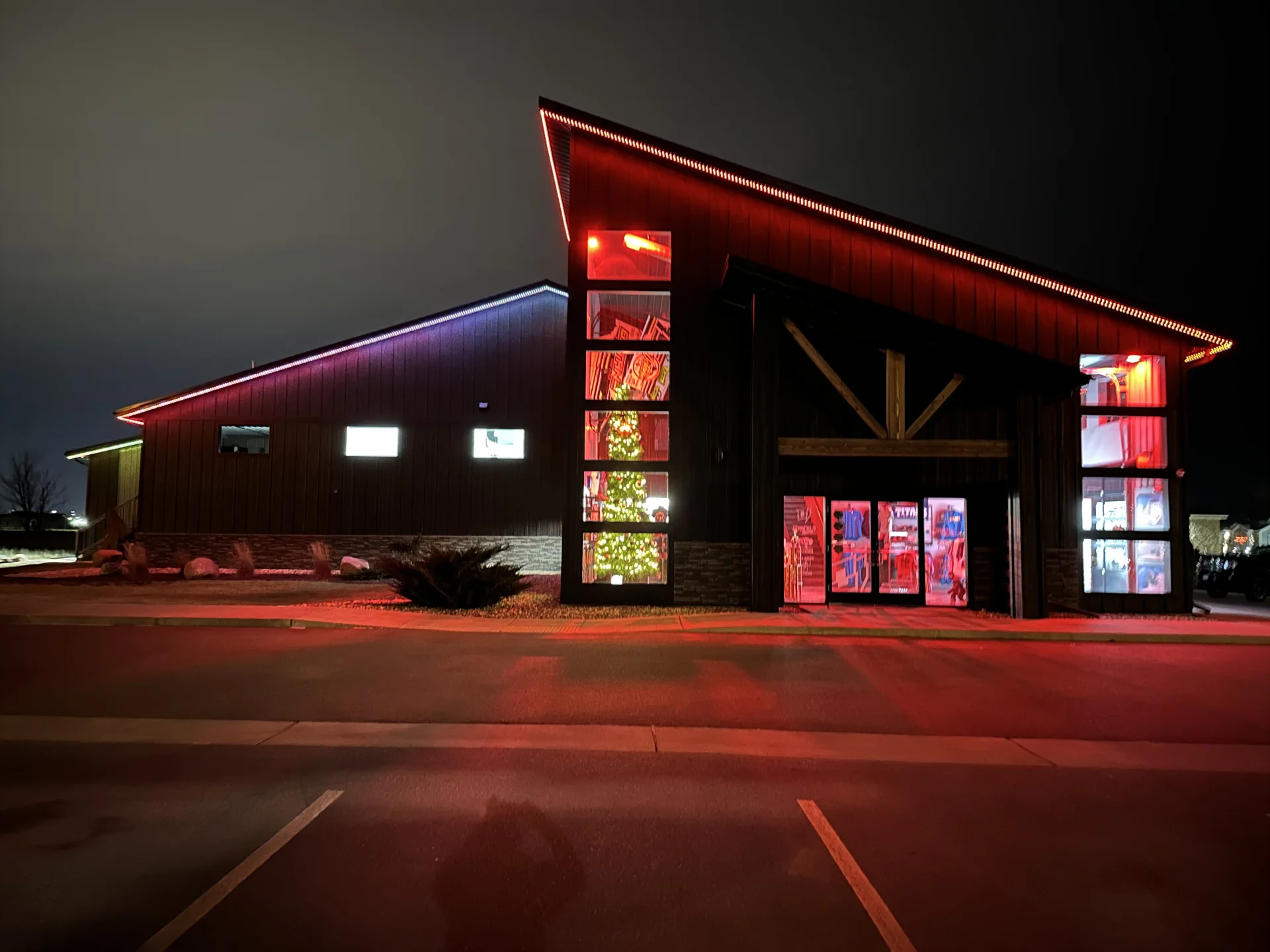 Modern building at night with red neon accent lighting and illuminated windows in a parking lot