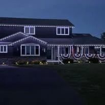 Two-story house at dusk outlined with white holiday lights and red-white bunting on the porch