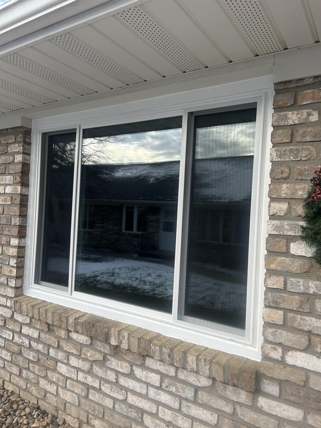 White-framed window on a brick house exterior with white soffit and siding reflection in the glass