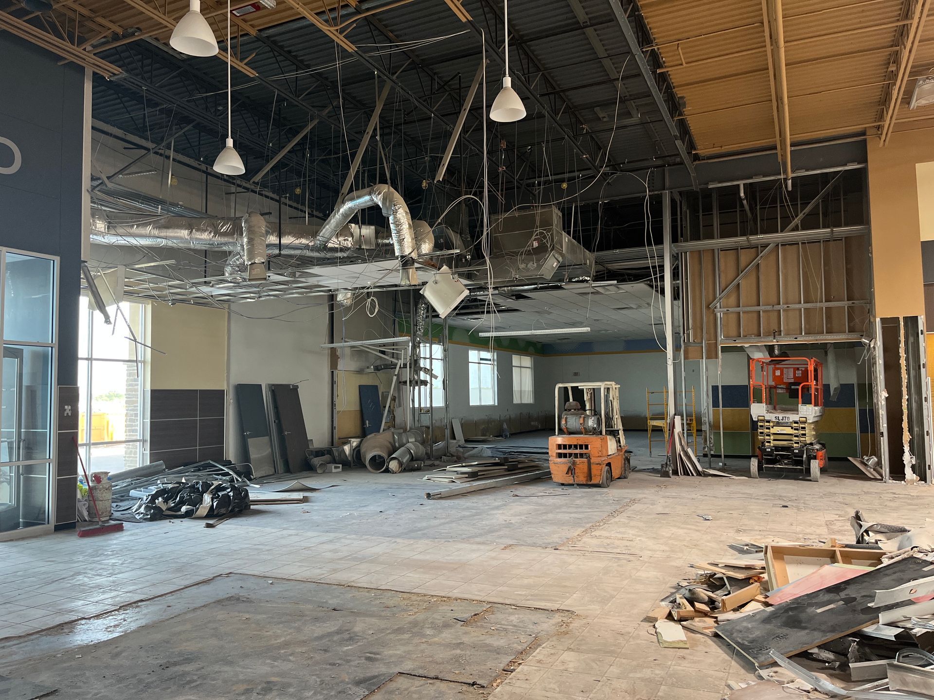 Interior demolition scene. Damaged ceiling, debris on floor, forklift, and construction equipment.