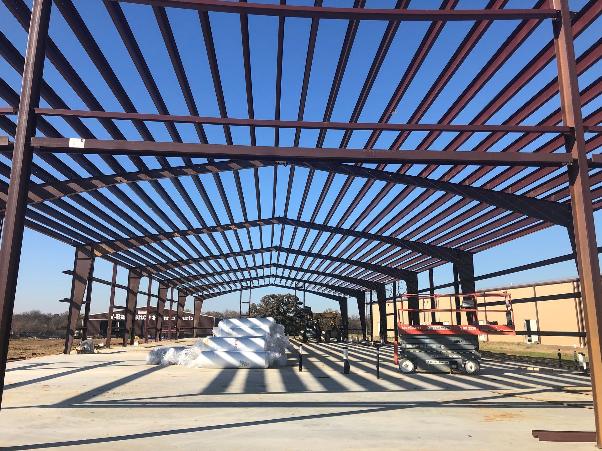 Steel frame of a building under construction, brown beams against a blue sky.