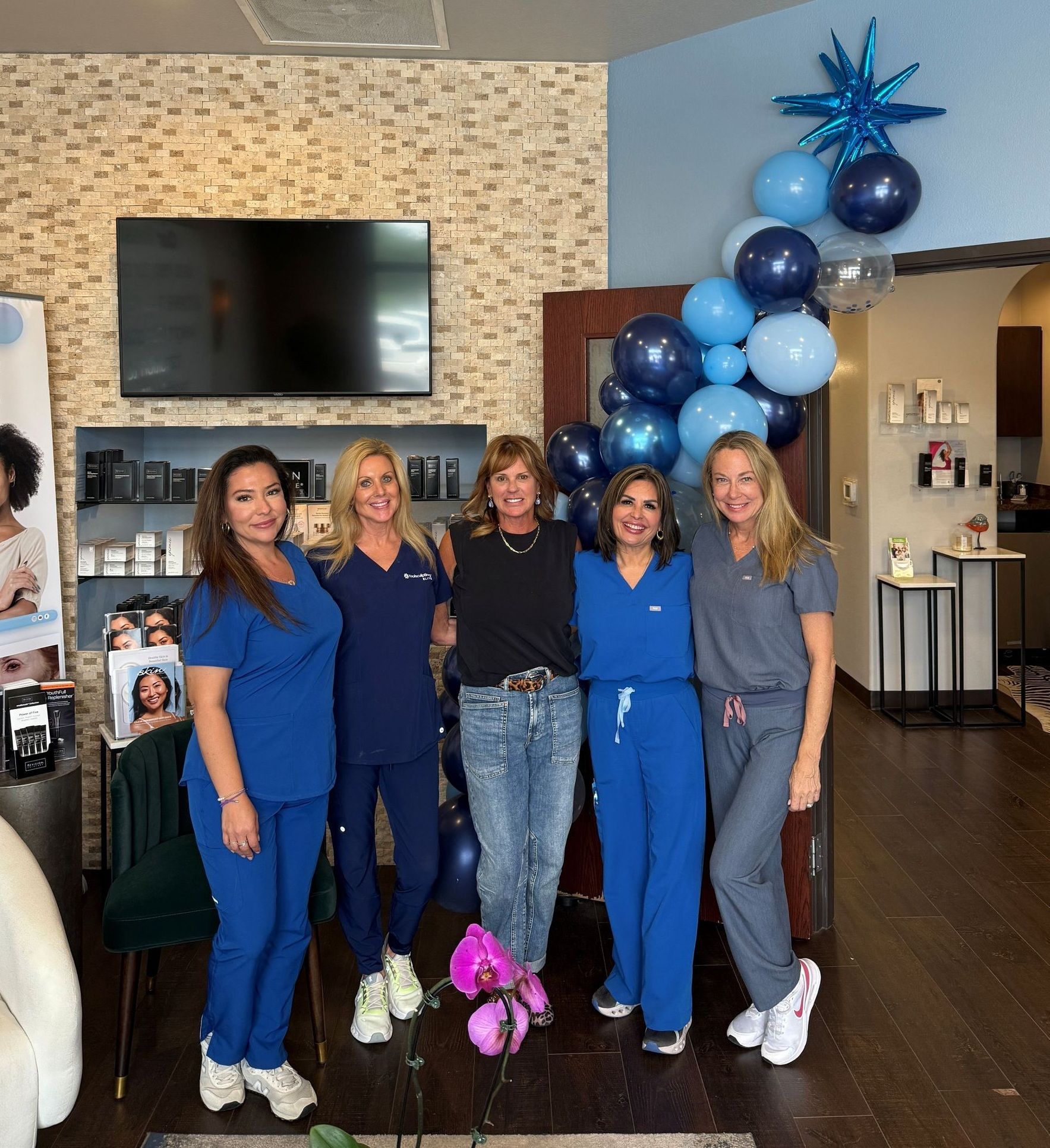 Five people in blue scrubs. Balloons and floral arrangement in setting.