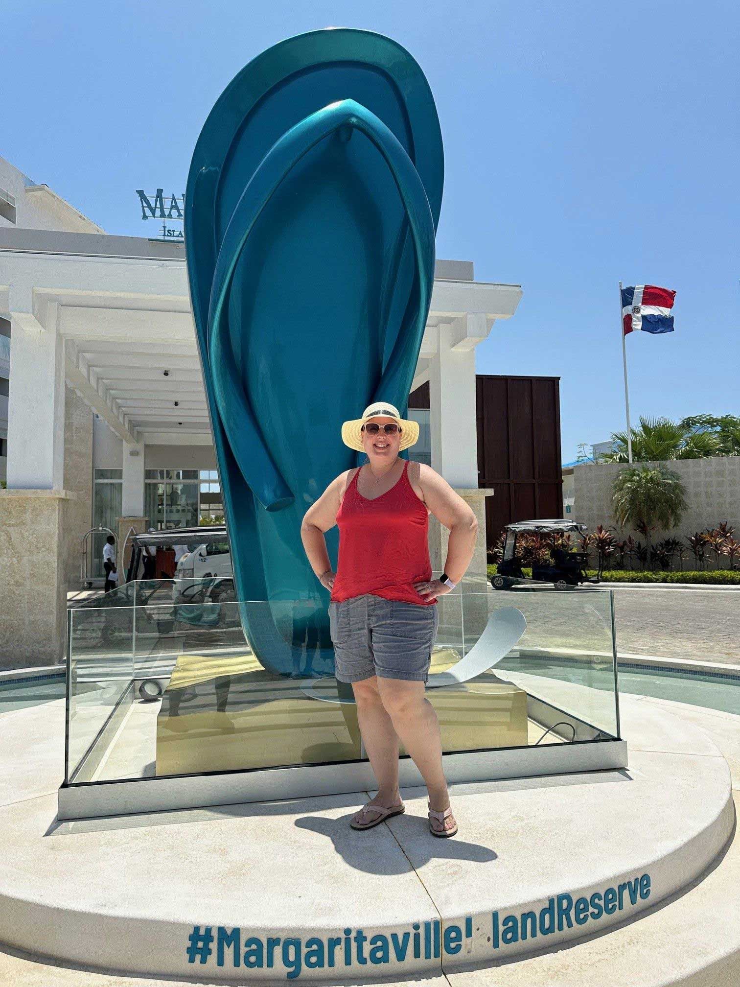 a woman stands next to a giant teal flip-flop statue