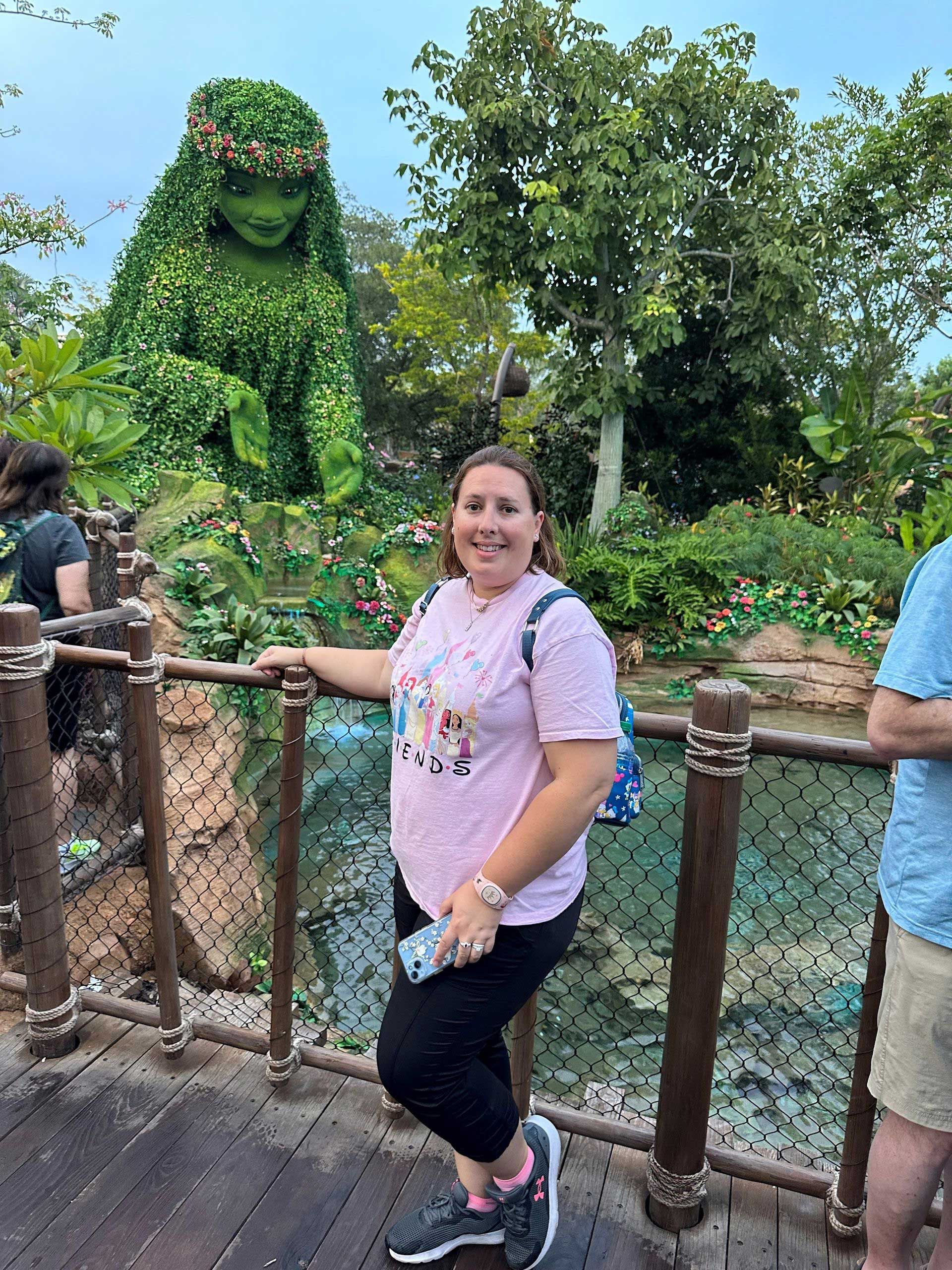 a woman poses on a bridge in front of a lush plant sculpture of Te Fiti