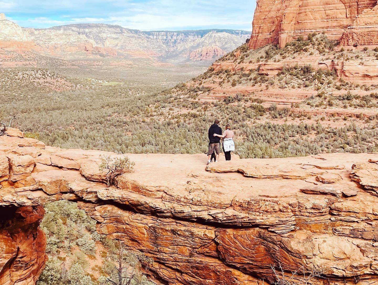A man and a woman are standing on top of a rocky cliff.