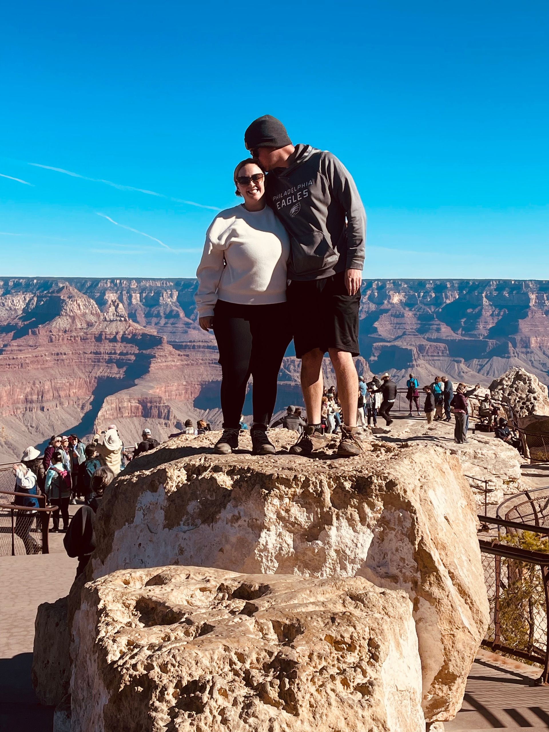 A man and a woman are standing on top of a large rock.