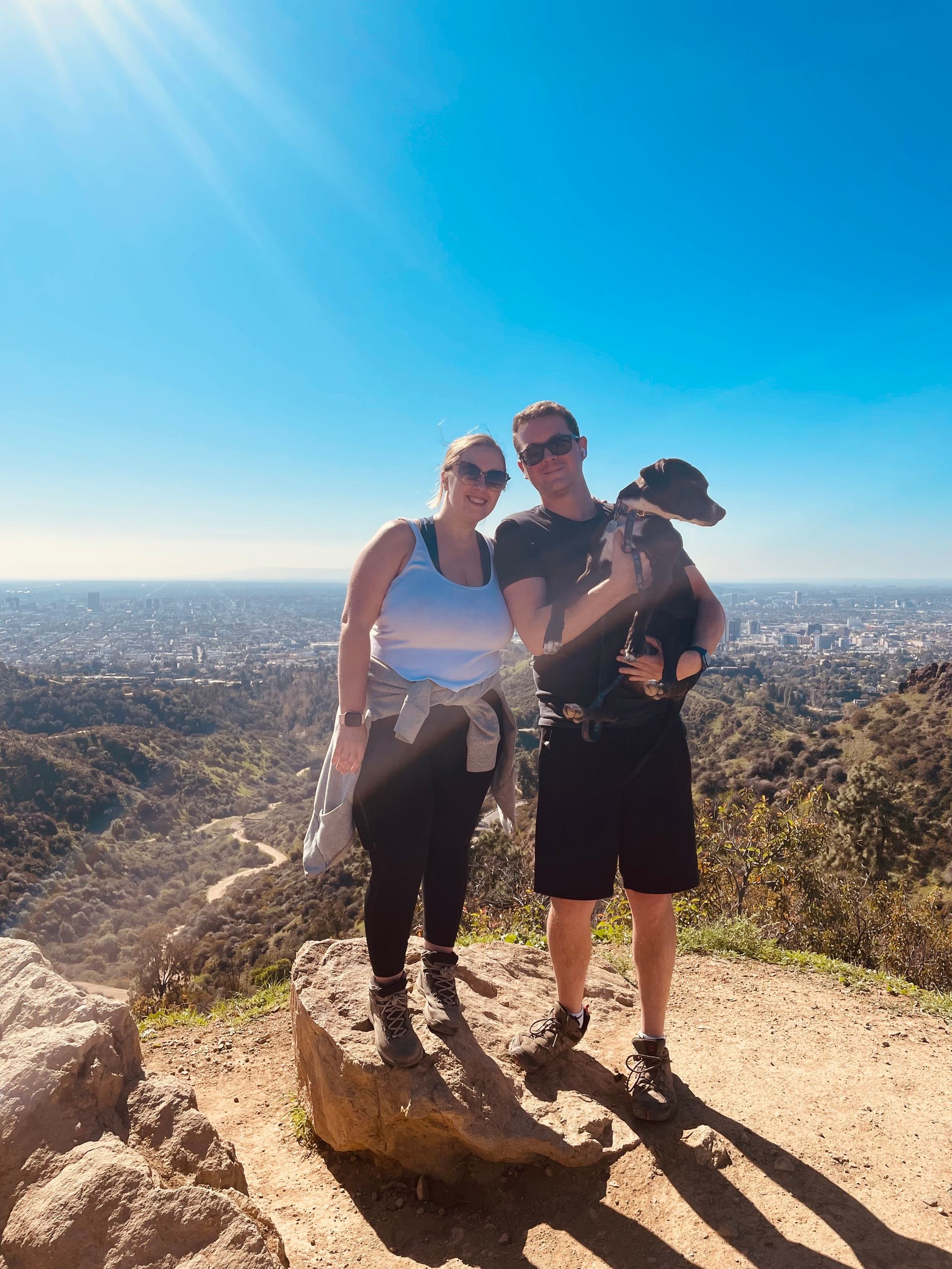 A man and a woman are standing on top of a rock holding a dog.