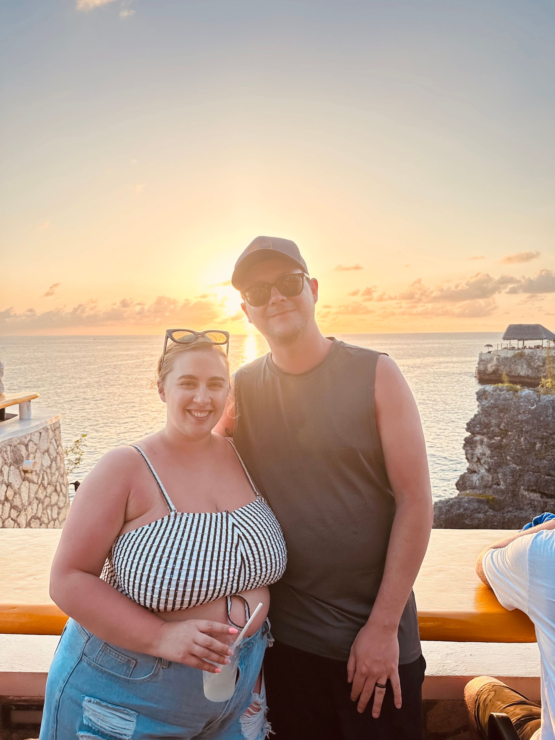 A man and a woman are posing for a picture in front of the ocean at sunset.
