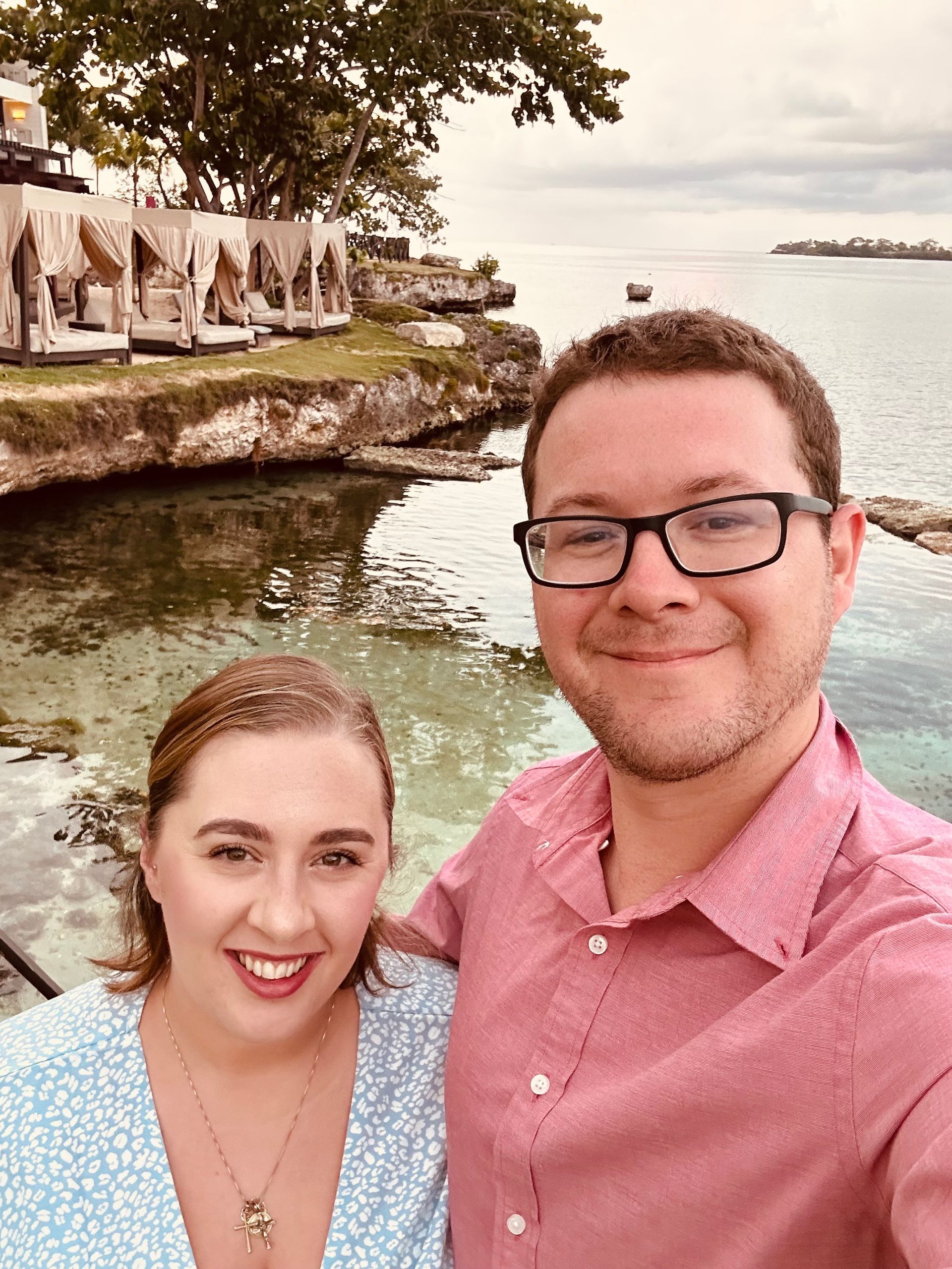 A man and a woman are posing for a picture in front of the ocean.