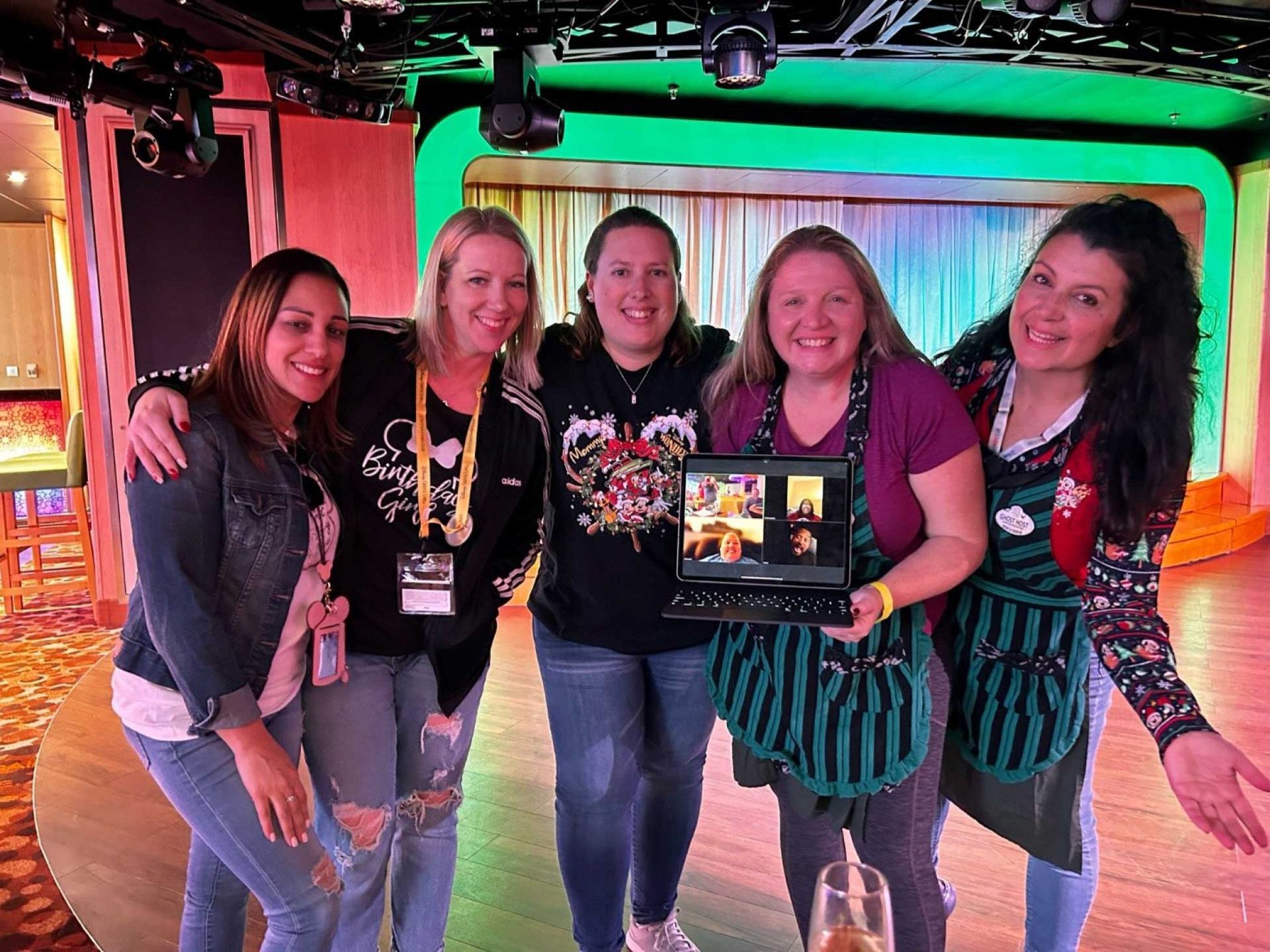 five women smiling and posing with a laptop showing a video call
