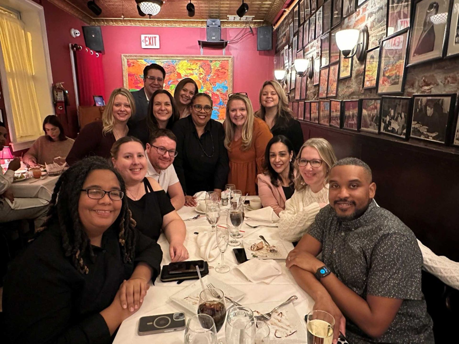 a group of people around a restaurant table The setting is a warmly lit room with artwork and framed photos on the walls.