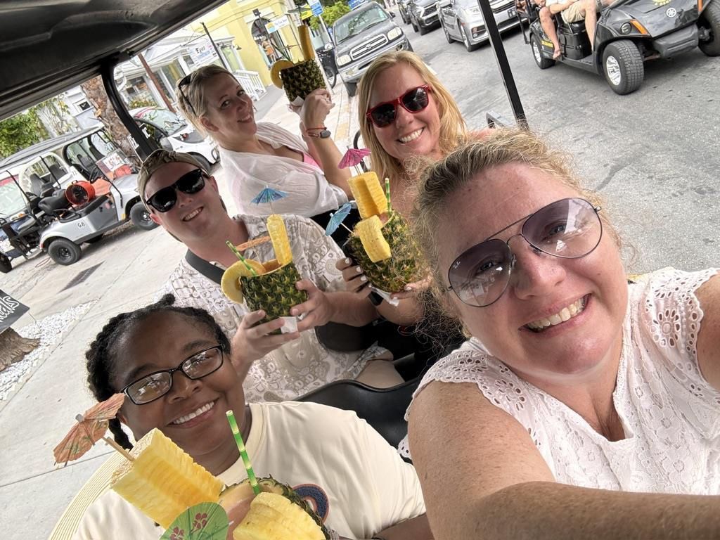 A group of women are sitting in a golf cart holding pineapples.