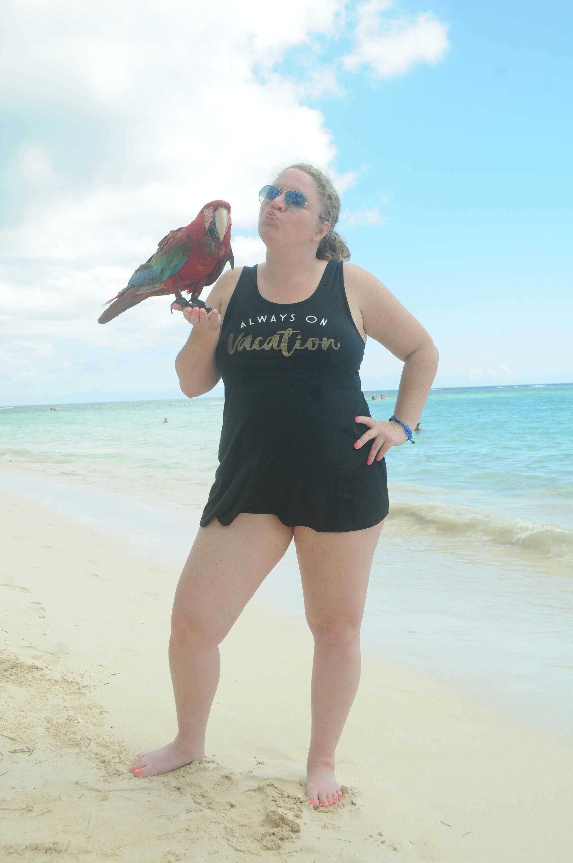 woman on a beach with a macaw perched on her hand