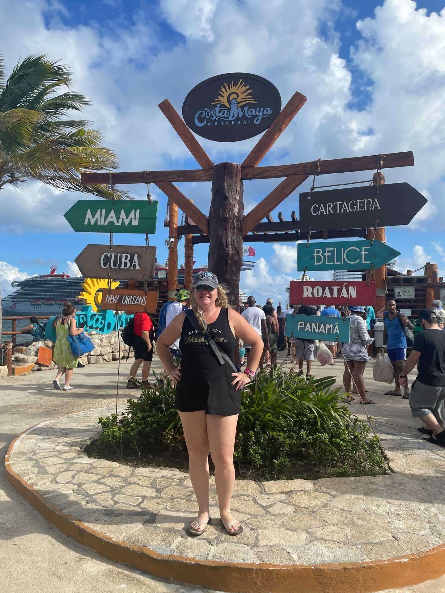 a woman stands by a signpost at Costa Maya pointing to various destinations
