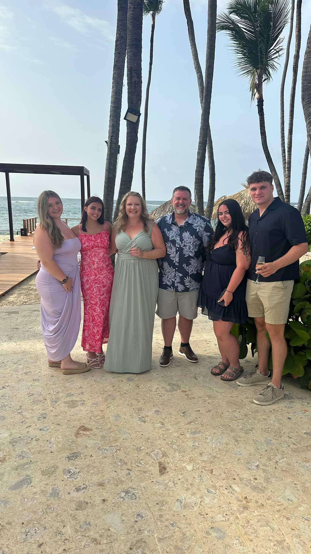 a group of six people posing for a photo on a beach with palm trees, the sky in the background