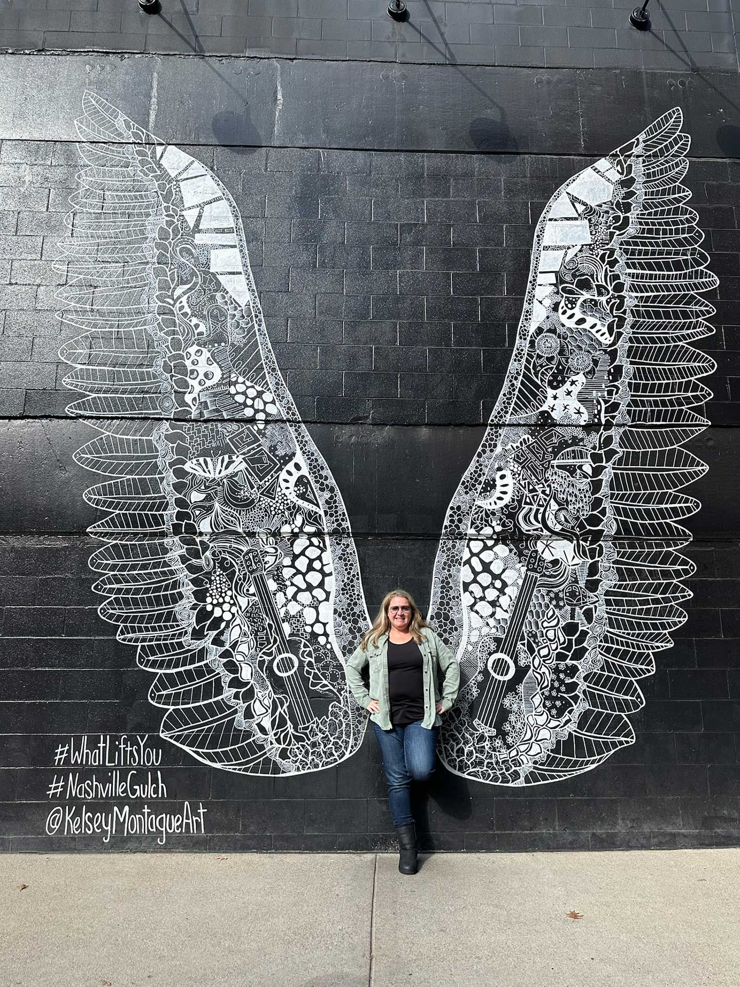 a woman stands in front of a black and white angel wing mural