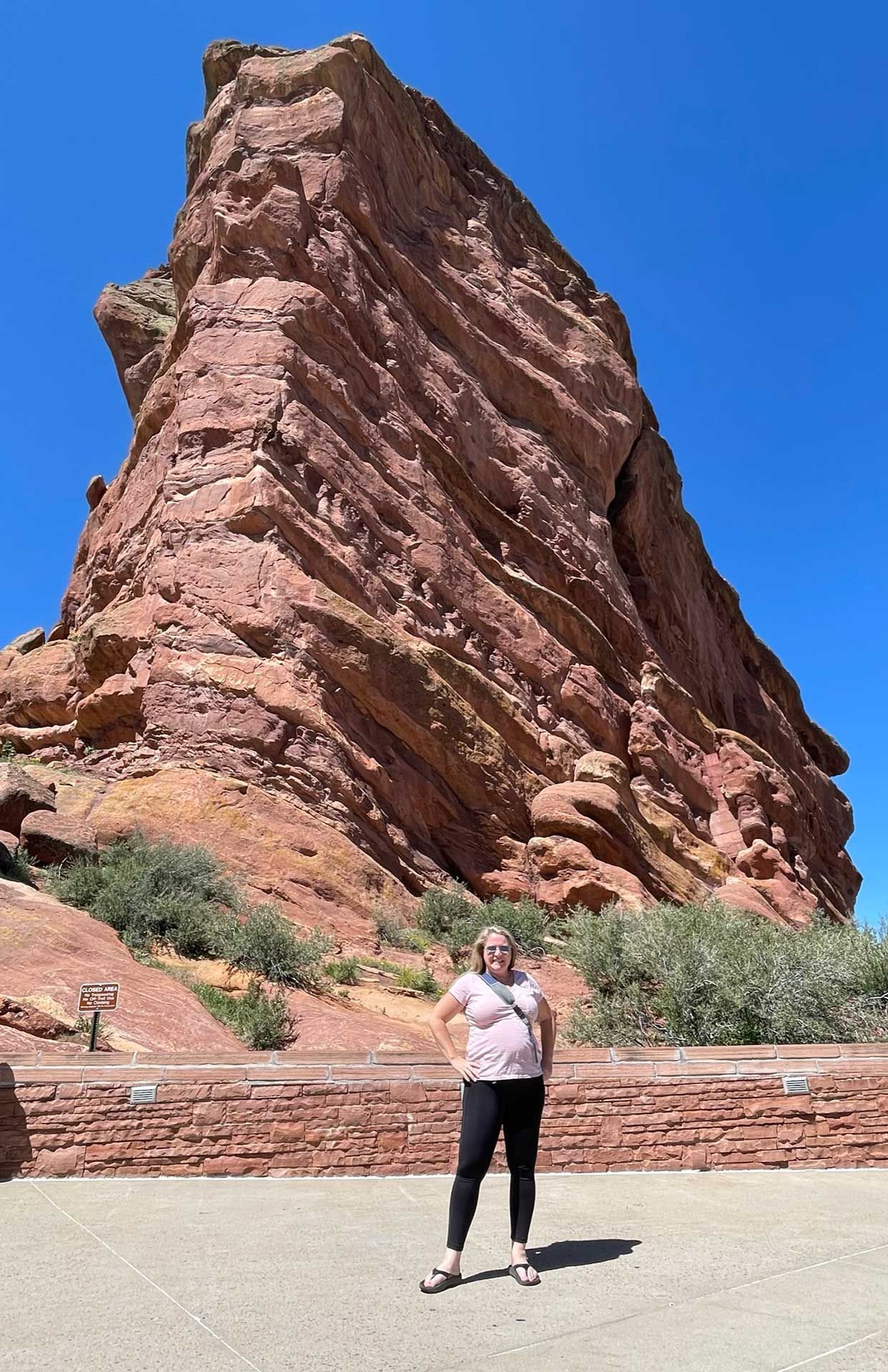a woman stands smiling in front of a large, red rock formation